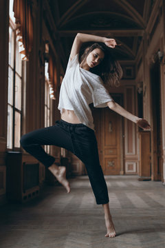 Full height of barefoot skinny dancer in long theatre corridor. Dynamic photo of brunette sexy ballerina girl dancing in classic museum interior. Contemporary dance