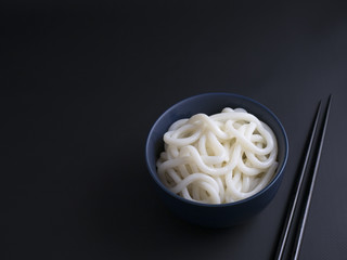 Cooked udon noodles from Korea in small blue bowl, isolated on black background