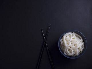Cooked udon noodles from Korea in small blue bowl, isolated on black background