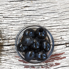 Delicious olives in a glass bowl on a wooden background. Ingredients of Italian and Mediterranean cuisine.
