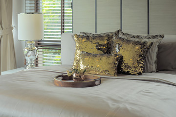 Wooden tray with golden glitter pillows on bed