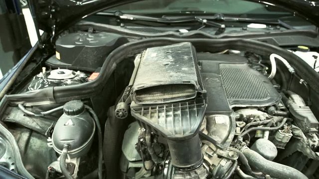 A man in gloves gently pulls out the air filter for replacement. He holds the device to protect the engine dust and dirt while driving on the road with both hands. As the unit becomes clogged, its