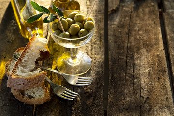 Glass glass filled with olives and bottles of olive oil on the rustic table