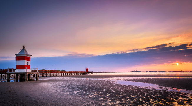 Beautiful sunrise at the seaside in Italy, at Lignano Sabbiadoro, with pier and lighthouse in the foreground.