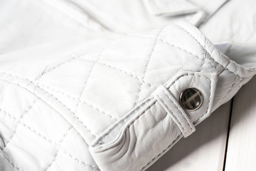 Metal clasp button on white leather jacket.  Leather jacket shoulder detail. White background. Macro detail