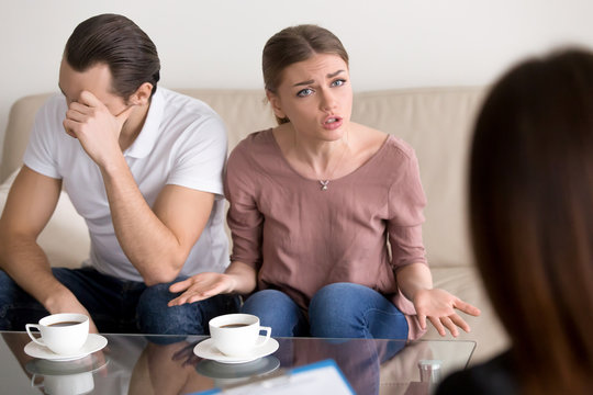 Portrait of unhappy couple consulting marriage counselor or family psychologist. Young emotional woman telling specialist about problems, her husband sitting next to wife frustrated and depressed