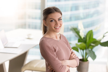 Head shot portrait of happy smiling young businesswoman standing with arms crossed, looking at...