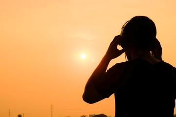 Man silhouette listening to the headphones on the sunset landscape background.