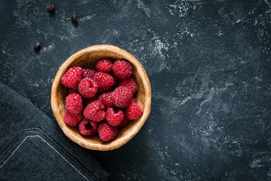 Fresh raspberries in bowl on dark stone background with copy space. Top view
