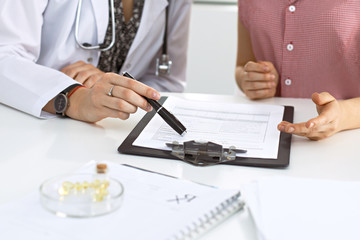 Doctor and patient sitting at the desk. Physician pointing into medical history records and explaining something to young woman. Medicine and health care concept.