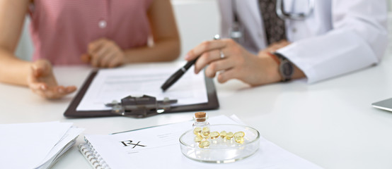 Obraz na płótnie Canvas Medical prescription form, capsules and pills are lying against the background of a doctor and patient discussing health exam results.