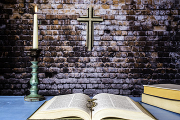 three bibles on blue table one open with reading glasses and lit candle in antique candle holder...