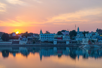 Obraz premium Cityscape at Pushkar, Rajasthan, India. Temples, buildings and ghats reflecting on the holy water of the lake at sunset.
