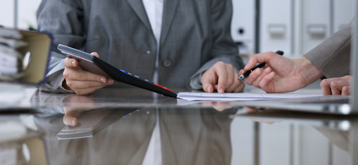 Two female accountants counting on calculator income for tax form completion, hands closeup. Internal Revenue Service inspector checking financial document. Planning budget, audit  concept.