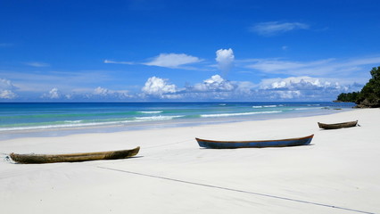 drei einfache Holzboote liegen malerisch am weiten weißen Strand am blauen Meer
