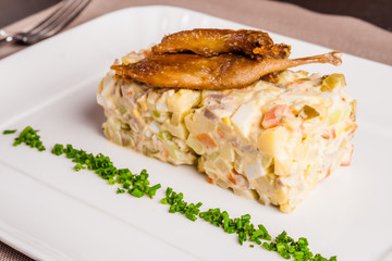 Olivier salad with quail on white plate