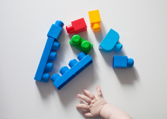 Close up of child's hands playing with colorful plastic bricks at the table. Toddler having fun and building out of bright constructor bricks. Early learning