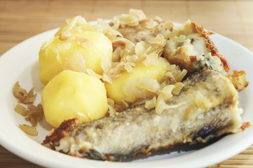 Fried fish and boiled potatoes lies on a plate on a bamboo napkin. Close-up, selective focus.