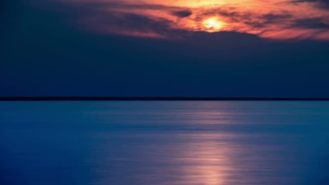 Time lapse of dusk with moving dark clouds above lake with sun rays reflections.