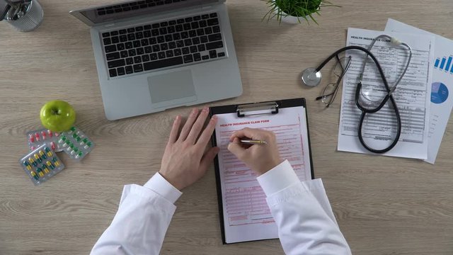 Top view of general practitioner filling health insurance claim form, healthcare