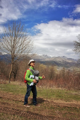 Young father with infant baby in sling carrier hiking in Armenian mountains.