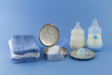 Baby boy luxurious items collection isolated on pale blue background. Silver can with hairbrush and comb. Pacifier on a silver plate, milkbottles and towels.