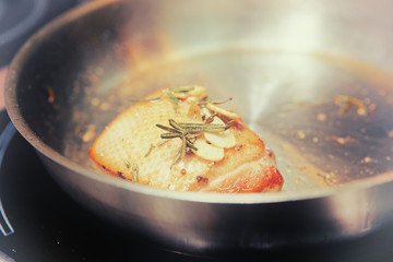 Duck breast being fried in pan with herbs, toned
