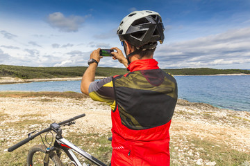 Naklejka premium Mountainbiker am Meer macht ein Foto mit dem Smartphone