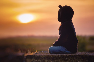 Silhouette of Kid sitting on the stone watching the sunset or sunrise summer time in twilight, Happiness and Enjoy Life Concept.