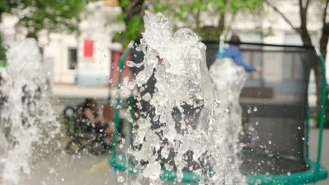 Park fountain in slomo with defocused kid jumping on background
