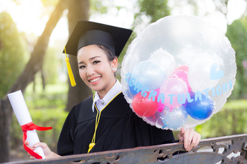 Portrait of happy young female graduates in academic dress and square academic cap holding word...