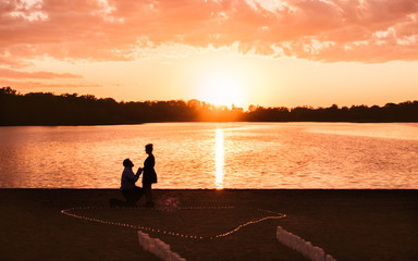 Fototapeta premium A man is proposing to his girl friend at a lake under sunset