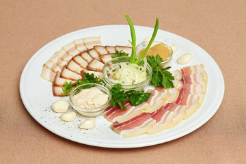 Strips of bacon and sliced lard, sauce, greens on plate