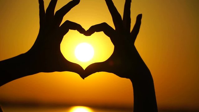 Woman makes heart and hands directs the sunset