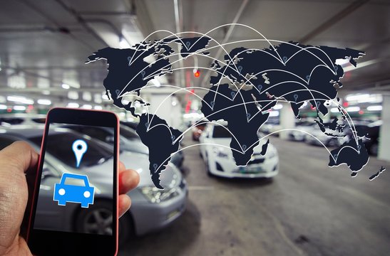 hand holding smart phone with car symbol and world map global connection in intelligent car park concept on blurred parking car indoor background, color tone effect.
