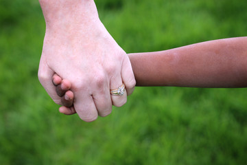 An African child holding his caucasian adoptive mother's hand.