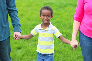 A young boy is holding hands between his caucasian, adopted mother and father.