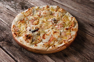 Appetizing hot baked pizza with cheese, bacon and ham served on wooden rustic table. Italian fast food, traditional cuisine.