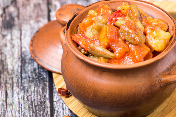  Vegetable stew. Stewed vegetables in a clay pot on an old wooden table. 