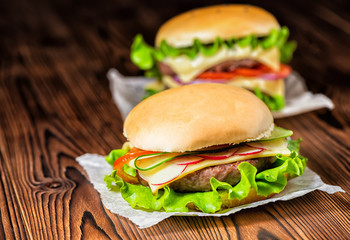 two homemade full cheeseburgers with vegetables, spices and beef meat on dark wooden background, copy space