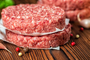raw ground beef meat hamburger patties on paper, dry pepper and garlic on wooden background