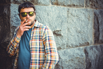 A man, a resident of a large metropolis, leads an unhealthy lifestyle, stands and smokes cigarettes near a local bar