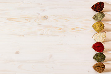 Various colorful powder seasoning close-up in paper corners on white wooden board with copy space.