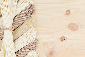 Sheaf raw asian noodles on soft beige wooden board with copy space, top view.