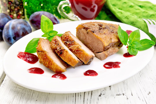 Duck breast with plum sauce and basil in plate on board