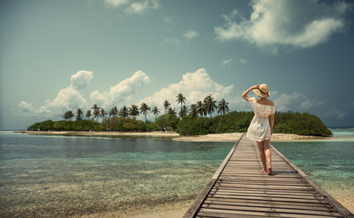 A girl in a white dress and hat is standing on a bridge. Maldives. Island. Tropics.