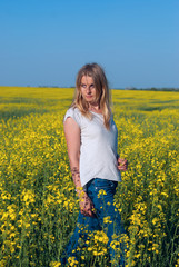 Naklejka na ściany i meble Beautiful young woman, blonde poses in a field of yellow flowers