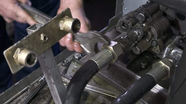 The worker tightens the nut with the key. Repair of hydraulic equipment. Hydraulic pressure hoses