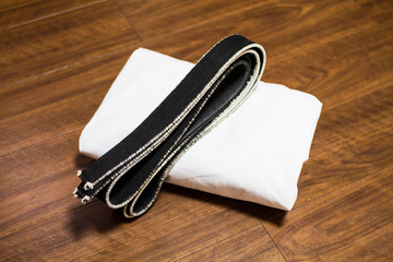 Black belt and Gi for martial arts ( Karate, Judo, Jiu-Jitsu, Kenpo, Taekwondo, Budo) on the wood...