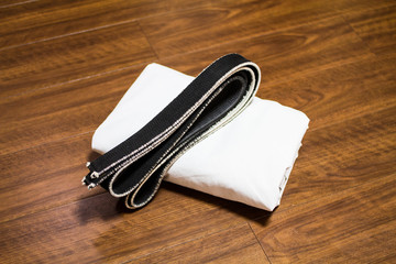 Black belt and Gi for martial arts ( Karate, Judo, Jiu-Jitsu, Kenpo, Taekwondo, Budo) on the wood...